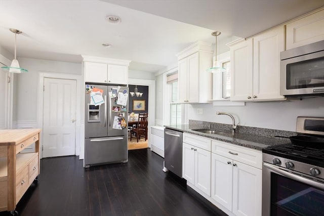 kitchen with stainless steel appliances, a sink, dark stone counters, white cabinets, and dark wood-style floors