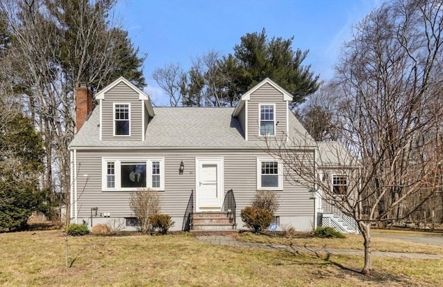 cape cod house with entry steps, a front yard, a shingled roof, and a chimney