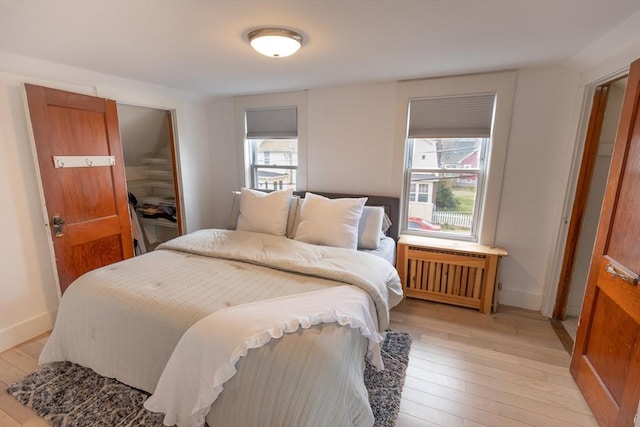 bedroom featuring radiator heating unit, baseboards, and light wood finished floors