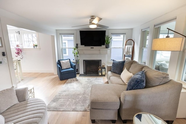 living room featuring baseboards, a fireplace with flush hearth, ceiling fan, and wood finished floors