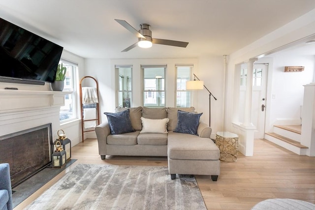 living room with a ceiling fan, baseboards, a fireplace with flush hearth, and light wood finished floors