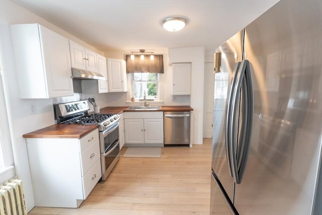 kitchen featuring butcher block countertops, light wood-style floors, radiator heating unit, white cabinets, and appliances with stainless steel finishes