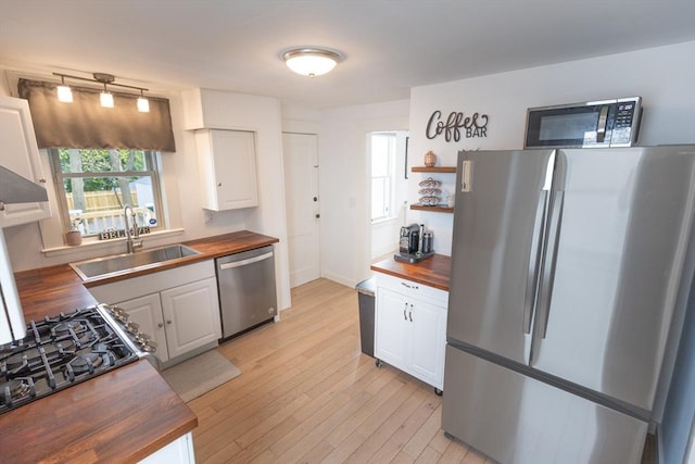 kitchen with a sink, appliances with stainless steel finishes, open shelves, and butcher block counters