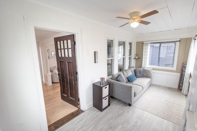 living area with light wood-style floors, ceiling fan, and crown molding