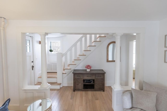 interior space featuring stairs, radiator, decorative columns, and light wood finished floors