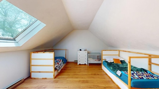 bedroom with baseboard heating, lofted ceiling, a skylight, and wood finished floors