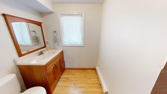 bathroom with a baseboard radiator, toilet, wood finished floors, vanity, and baseboards