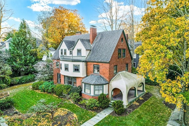 view of front of house featuring a front yard, a shingled roof, a chimney, and brick siding