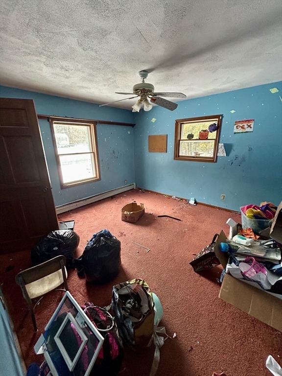 unfurnished bedroom with carpet flooring, a textured ceiling, ceiling fan, and a baseboard heating unit