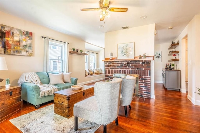 living area with wood finished floors, a ceiling fan, a brick fireplace, and baseboards