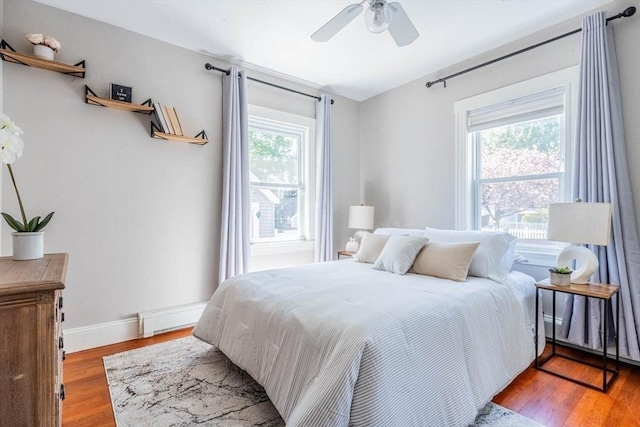 bedroom with wood finished floors, baseboards, a ceiling fan, and a baseboard heating unit
