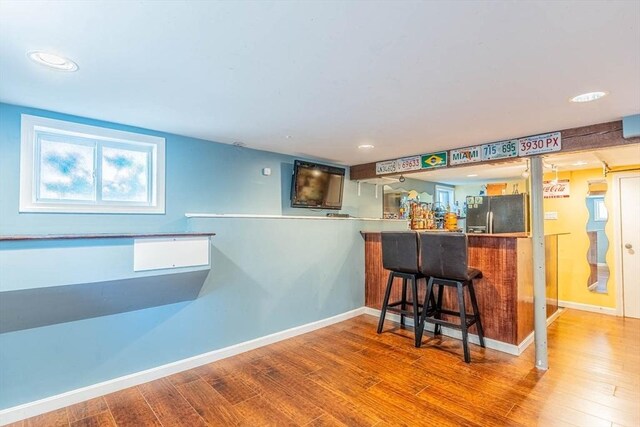 indoor dry bar featuring stainless steel refrigerator with ice dispenser, wood finished floors, baseboards, and recessed lighting