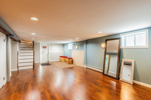 below grade area featuring a baseboard radiator, wood finished floors, recessed lighting, stairway, and plenty of natural light