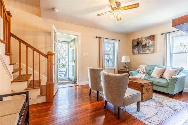 living room with dark wood-type flooring, ceiling fan, stairs, and baseboards
