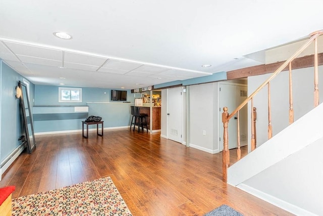 finished basement featuring stairs, wood finished floors, a baseboard radiator, recessed lighting, and baseboards