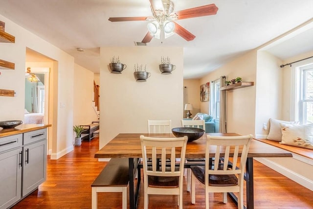 dining space with dark wood-style floors, ceiling fan, baseboards, and stairs