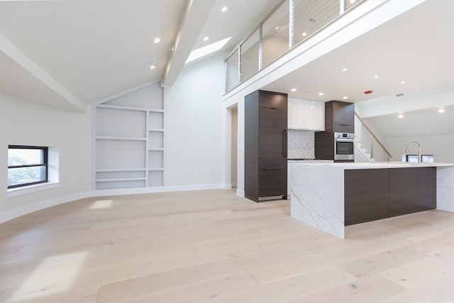 unfurnished living room with light hardwood / wood-style floors, high vaulted ceiling, a skylight, and built in shelves