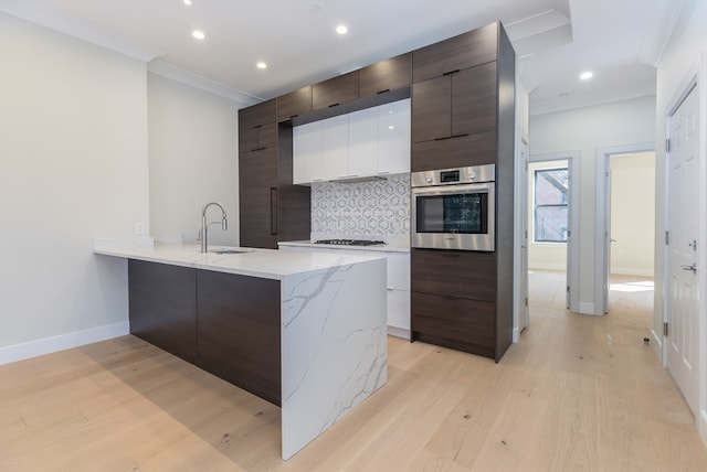 kitchen with tasteful backsplash, oven, sink, and light wood-type flooring