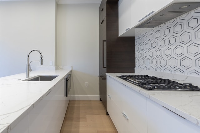 kitchen featuring light stone counters, white cabinetry, light hardwood / wood-style flooring, stainless steel gas cooktop, and sink