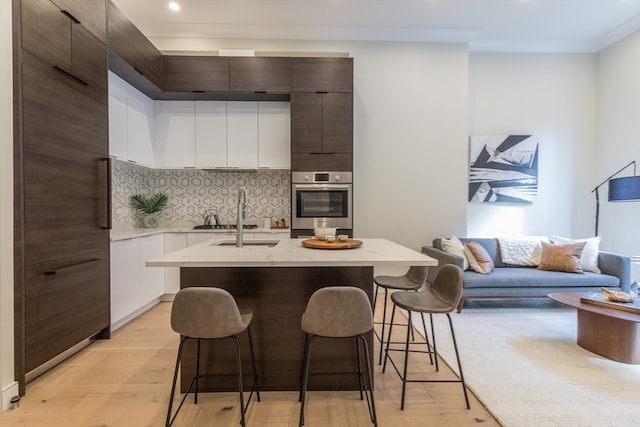 kitchen featuring white cabinets, stainless steel oven, a breakfast bar, a kitchen island with sink, and light hardwood / wood-style flooring