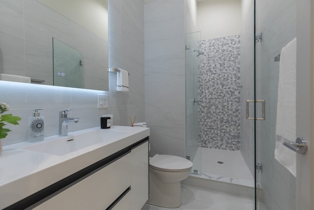 bathroom featuring tile patterned floors, toilet, vanity, tile walls, and walk in shower