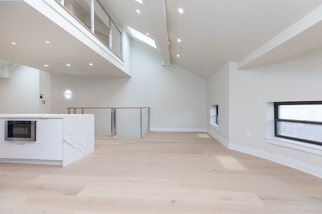 unfurnished living room with light hardwood / wood-style flooring, high vaulted ceiling, and a skylight