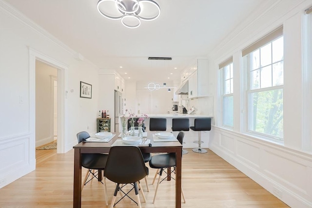 dining room featuring a decorative wall, crown molding, and light wood-style floors