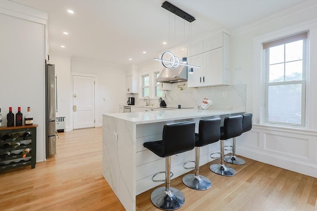 kitchen featuring a peninsula, white cabinets, light countertops, light wood-style flooring, and ornamental molding