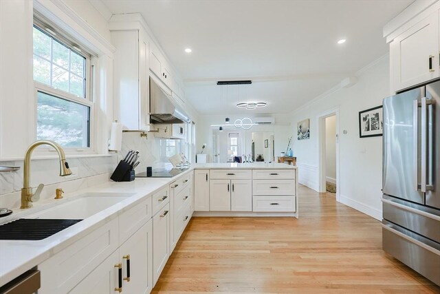 kitchen featuring freestanding refrigerator, under cabinet range hood, a sink, a peninsula, and white cabinets