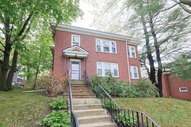 colonial-style house with brick siding, central air condition unit, and a front lawn