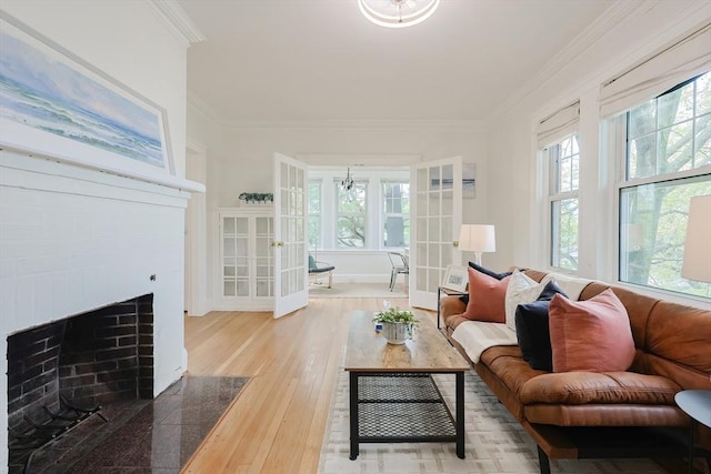 living area featuring a chandelier, wood finished floors, ornamental molding, a fireplace with flush hearth, and french doors