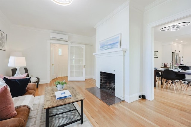 living room featuring a wall unit AC, a tiled fireplace, light wood-style floors, ornamental molding, and baseboards