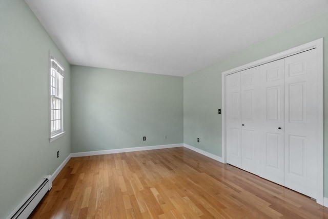 unfurnished bedroom with a closet, light wood-type flooring, a baseboard heating unit, and baseboards