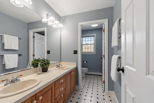 bathroom with a sink, toilet, baseboard heating, and double vanity