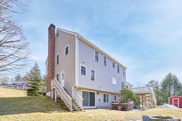 rear view of property featuring a shed, stairway, an outdoor structure, a chimney, and a hot tub