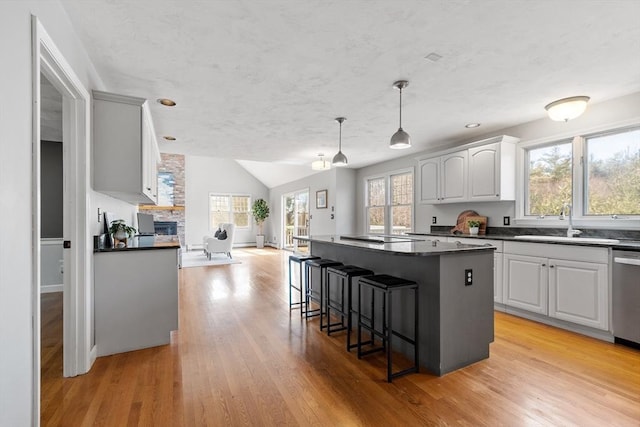 kitchen featuring light wood-type flooring, a sink, dark countertops, a breakfast bar area, and a fireplace