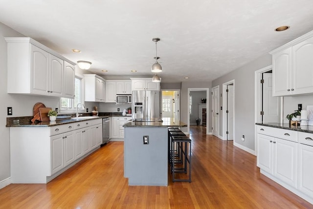 kitchen featuring a kitchen island, a breakfast bar, a sink, appliances with stainless steel finishes, and white cabinetry