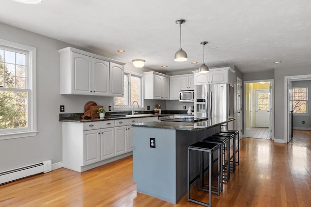 kitchen with baseboard heating, plenty of natural light, appliances with stainless steel finishes, and a kitchen breakfast bar