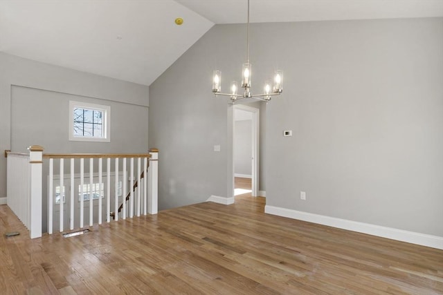 spare room with wood-type flooring, high vaulted ceiling, and a chandelier