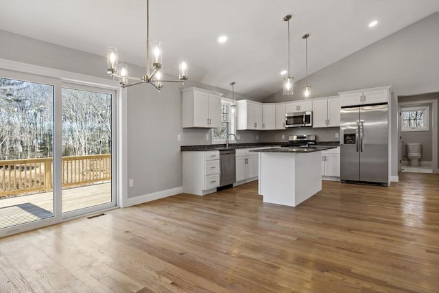 kitchen featuring decorative light fixtures, white cabinetry, a center island, stainless steel appliances, and light hardwood / wood-style flooring