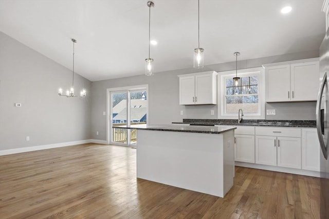 kitchen featuring hardwood / wood-style flooring, white cabinetry, hanging light fixtures, a kitchen island, and vaulted ceiling