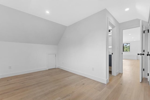 additional living space featuring vaulted ceiling and light wood-type flooring