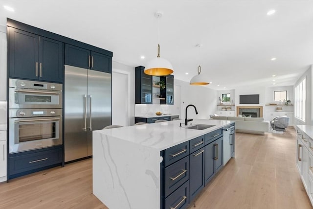 kitchen featuring sink, light stone counters, hanging light fixtures, a center island with sink, and stainless steel appliances