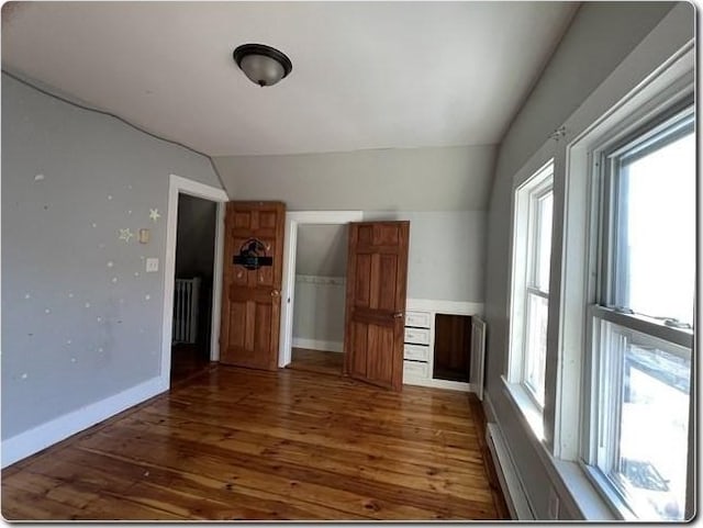 unfurnished living room with vaulted ceiling, dark hardwood / wood-style floors, and radiator