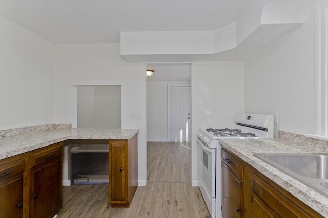 kitchen with white range with gas cooktop, sink, and light wood-type flooring