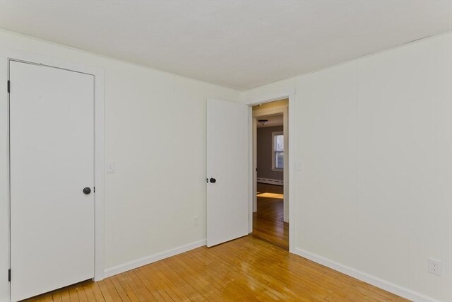 unfurnished bedroom featuring hardwood / wood-style flooring and a baseboard radiator