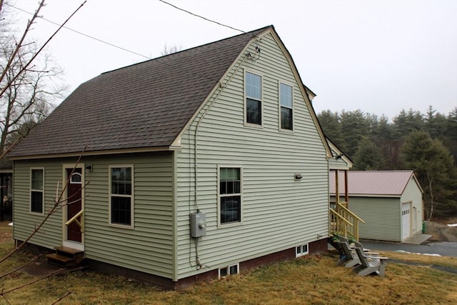rear view of property with a garage, roof with shingles, an outdoor structure, and entry steps
