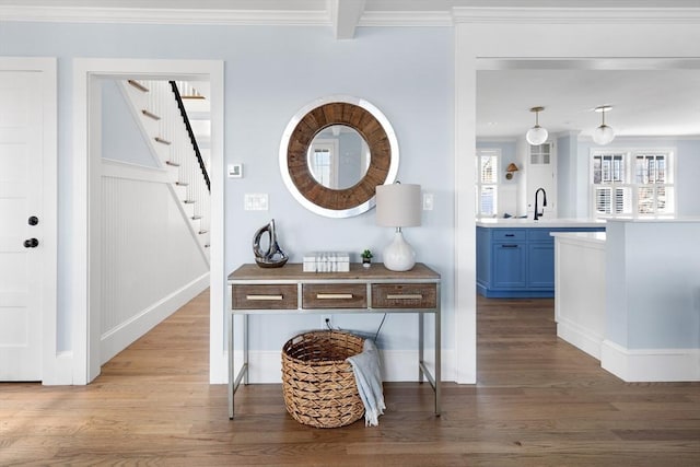 interior space with stairway, ornamental molding, wood finished floors, beam ceiling, and a sink