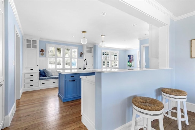 kitchen featuring light wood-style flooring, ornamental molding, a kitchen breakfast bar, blue cabinets, and light countertops