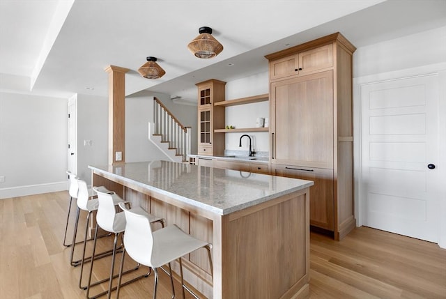 kitchen with light stone counters, open shelves, a sink, light wood-type flooring, and a kitchen breakfast bar